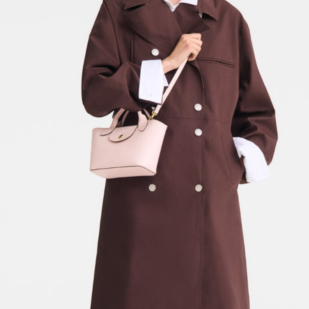 Lieblingstasche Epure XS light pink leather handbag with top handles and a crossbody strap, held by a woman in a brown coat.