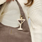 Lieblingstasche Espresso Martini charm hanging from a taupe suede hobo bag held by a person in a cream sweater.