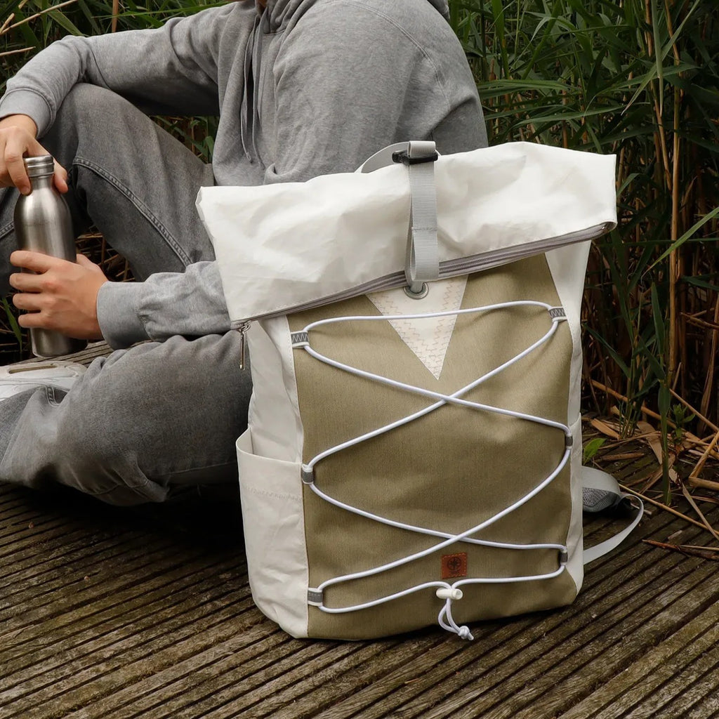 Lieblingstasche Fjord rolltop backpack in white and olive green with a front bungee cord system on a wooden dock.