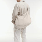 Lieblingstasche GOT BAG beige curved crossbody bag worn by a man in a matching light outfit against a white background