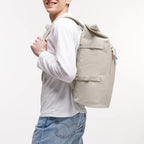 Man wearing a beige Lieblingstasche GOT BAG Rolltop 2.0 backpack with adjustable straps against a white background
