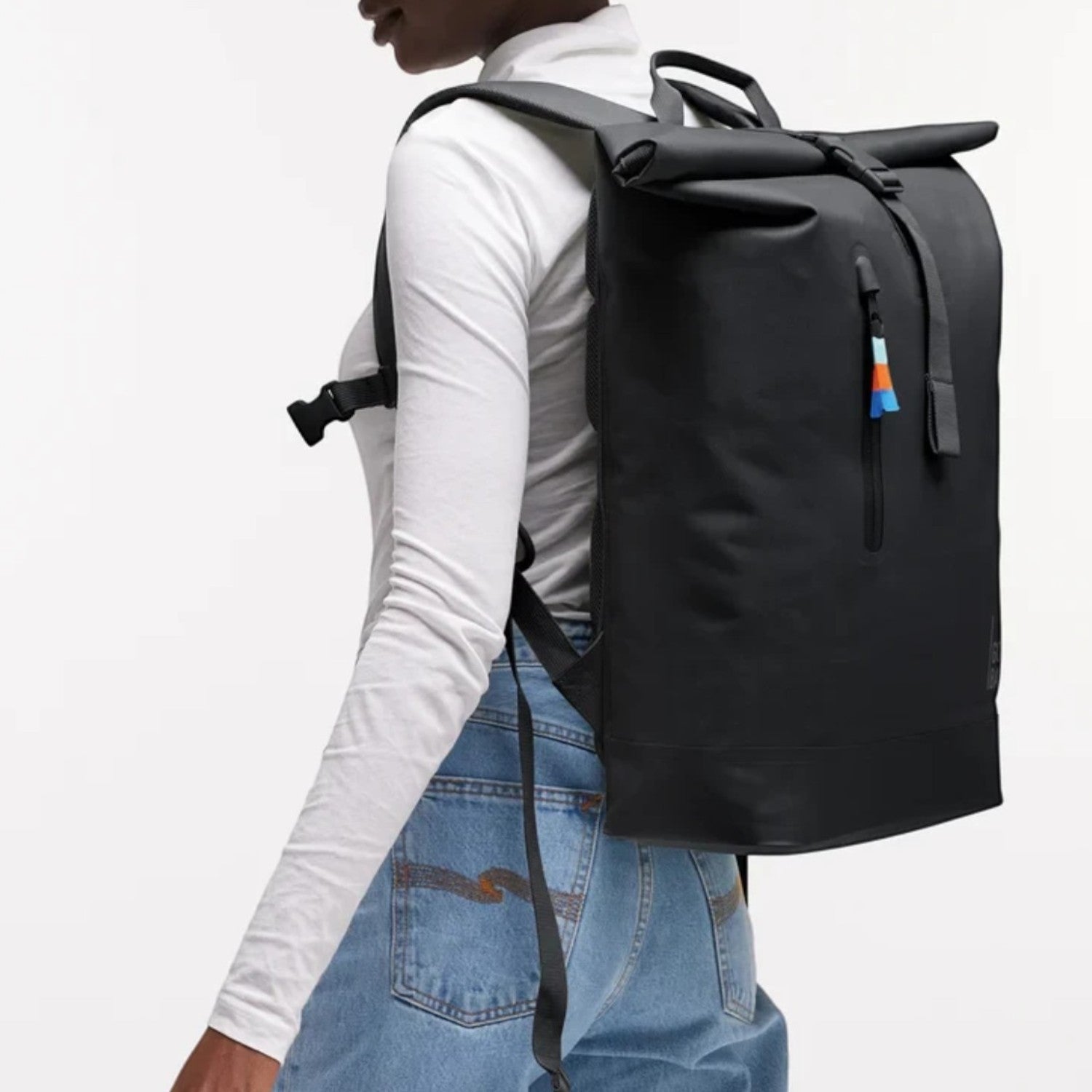 Model wearing a black Lieblingstasche GOT BAG Rolltop Lite 2.0 backpack with magnetic closure and adjustable straps.