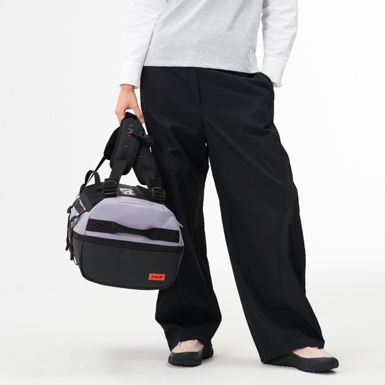 Model holding a Lieblingstasche grey and black duffel pack with adjustable straps against a white background