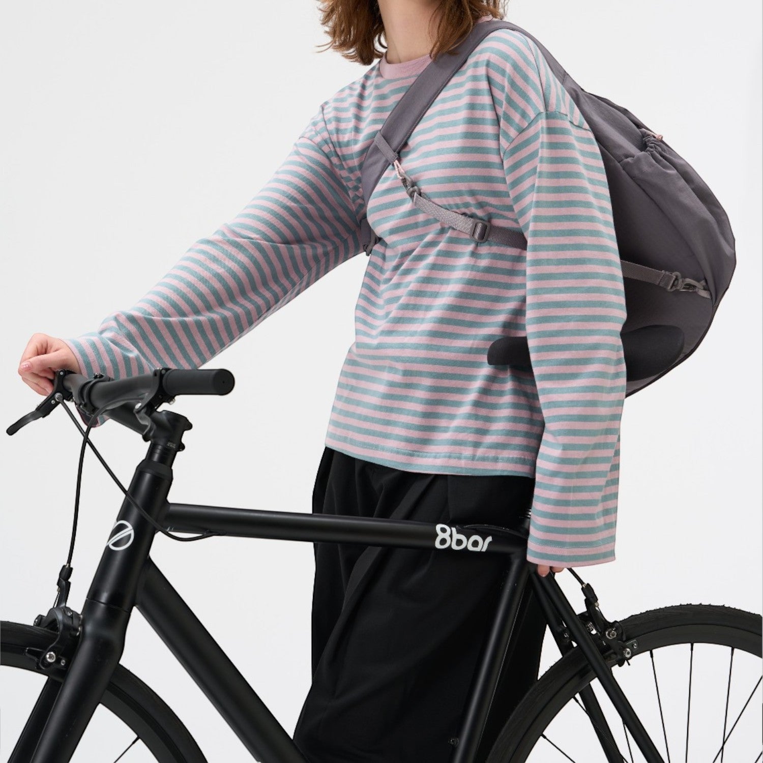 Lieblingstasche slouchy grey crossbody bag worn by a woman in a striped long-sleeve shirt riding a black bicycle
