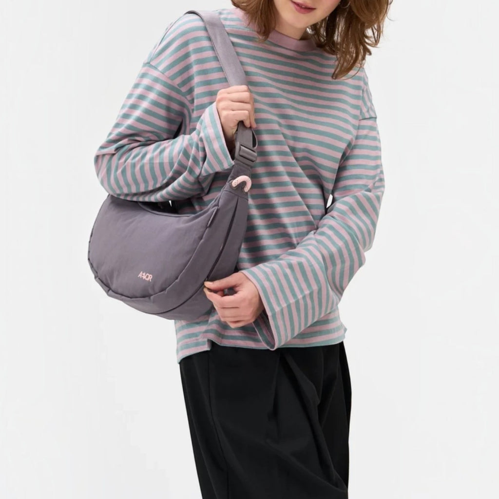 Lieblingstasche grey water-resistant sling bag worn as a crossbody by a woman in a striped long-sleeve shirt
