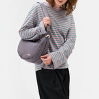 Lieblingstasche grey water-resistant sling bag worn as a crossbody by a woman in a striped long-sleeve shirt