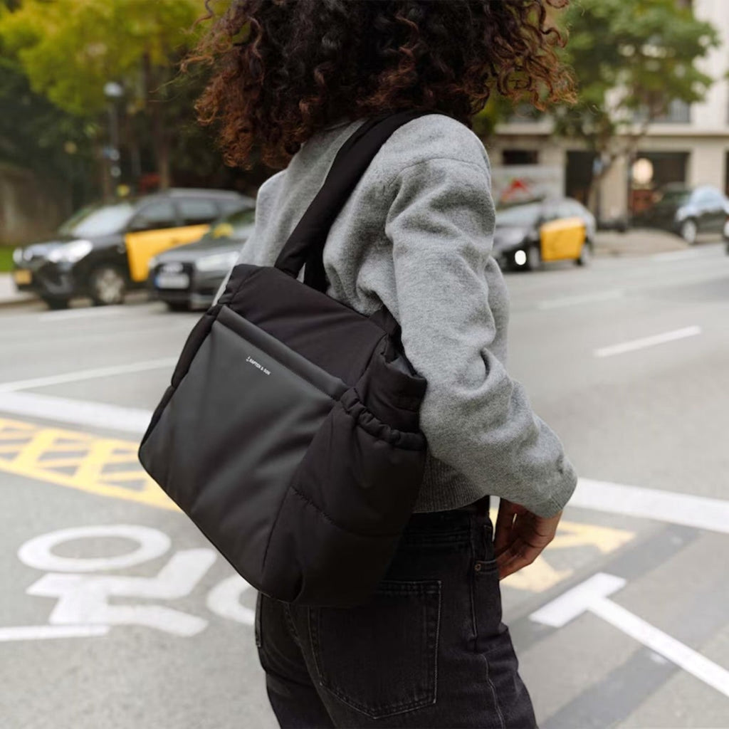 Lieblingstasche Hellvi Cloud Medium black padded shoulder bag with side bottle pockets worn by a woman in the city