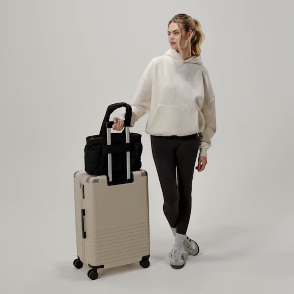 Lieblingstasche Hellvi Cloud Medium black quilted bag attached to a beige suitcase, held by a woman in casual wear.