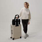 Lieblingstasche Hellvi Cloud Medium black quilted bag attached to a beige suitcase, held by a woman in casual wear.