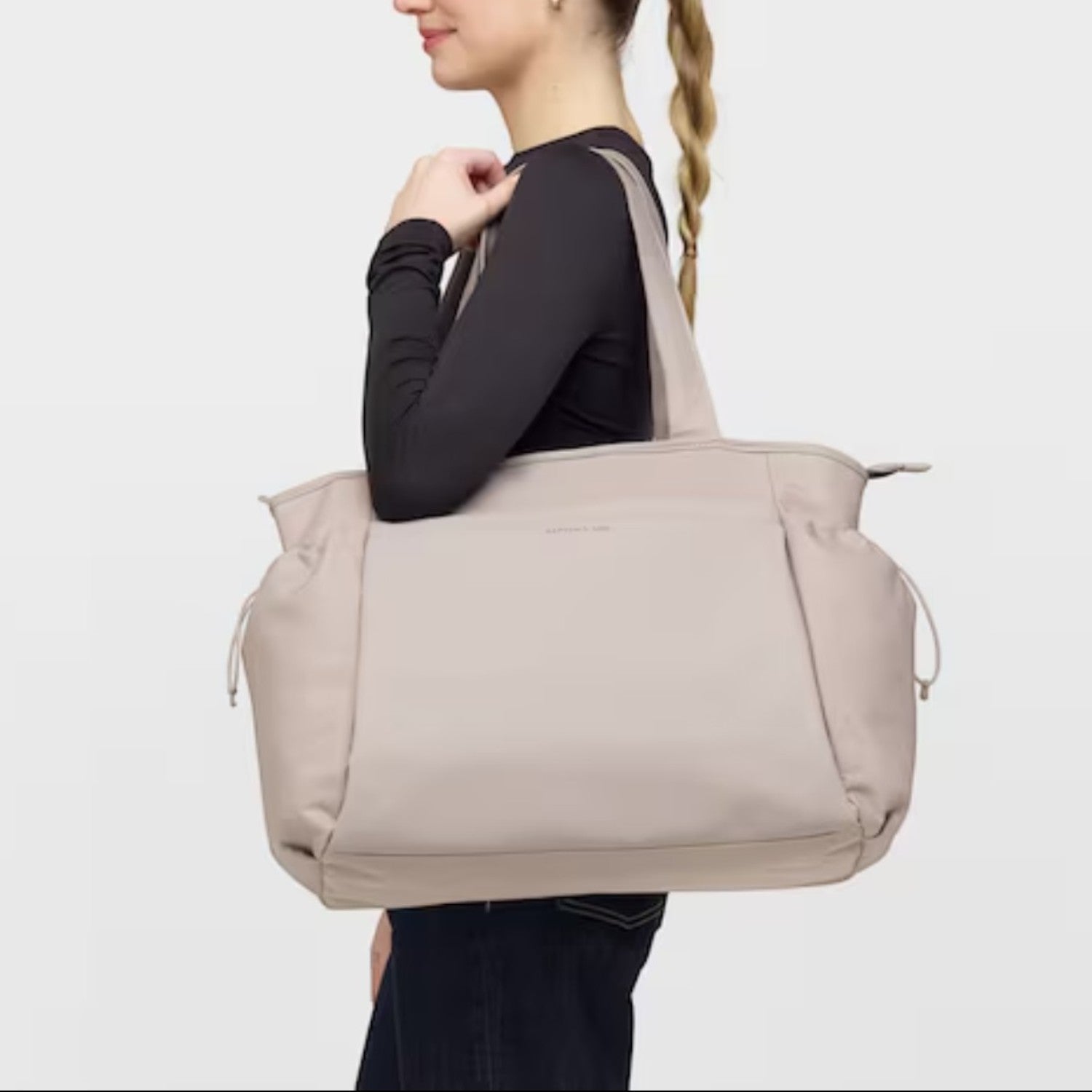 A woman carrying a large beige Lieblingstasche Hellvi Pro tote bag on her shoulder against a plain background.