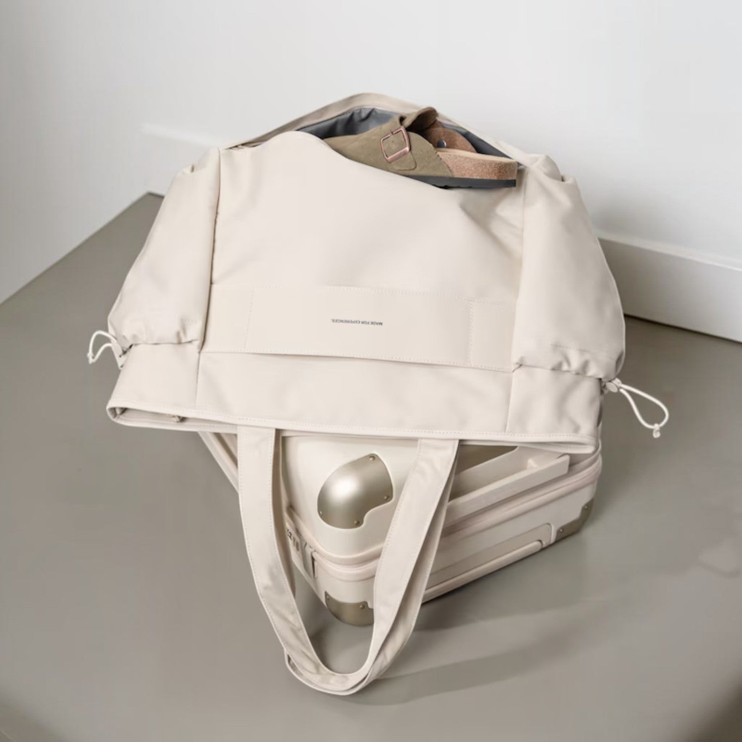 Lieblingstasche Hellvi Pro Large beige travel tote bag with drawstring sides resting on a matching suitcase