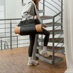 Lieblingstasche Hellvi Pro Large black sports bag carried by a woman walking up a spiral staircase with a yoga mat.