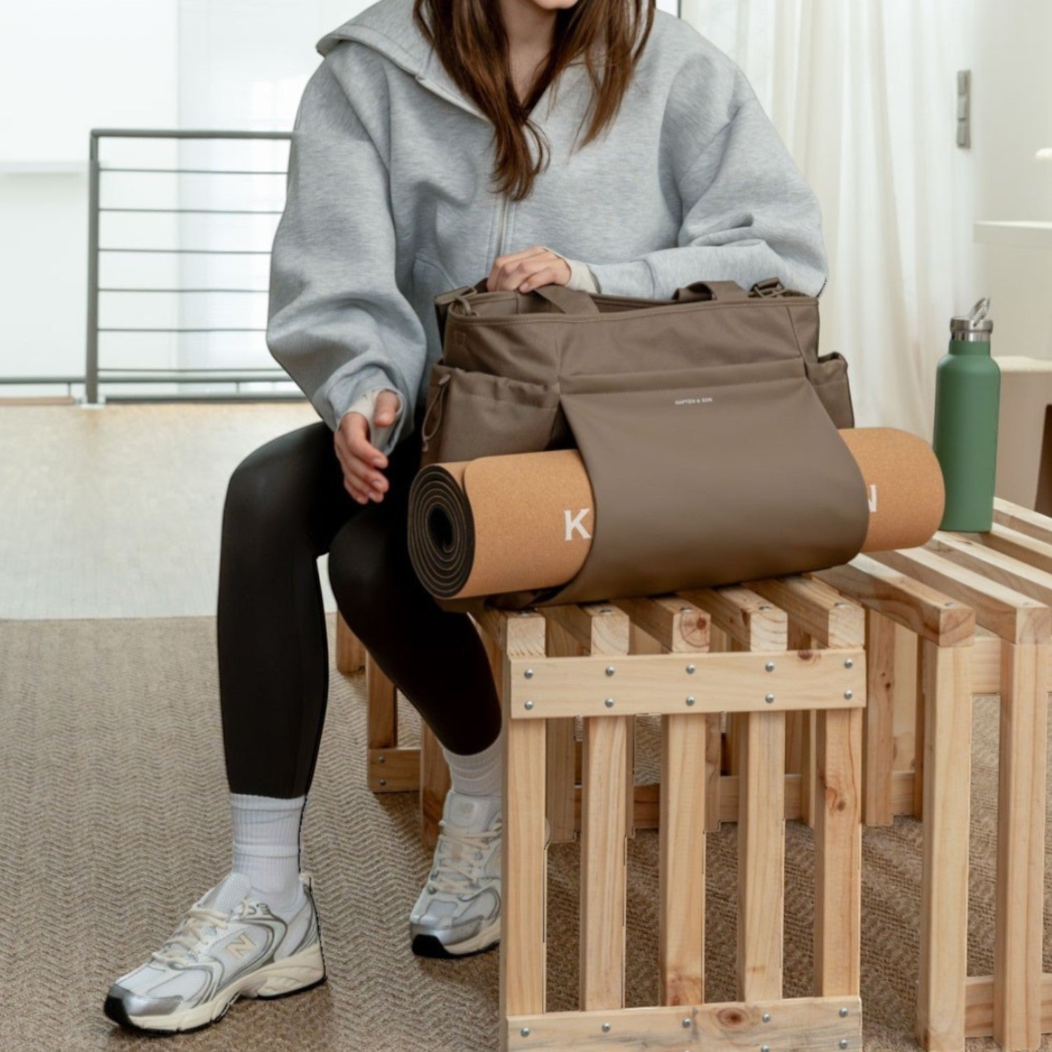 Lieblingstasche Hellvi Pro Large taupe sports bag with yoga mat holder, worn by a woman in a bright studio setting.