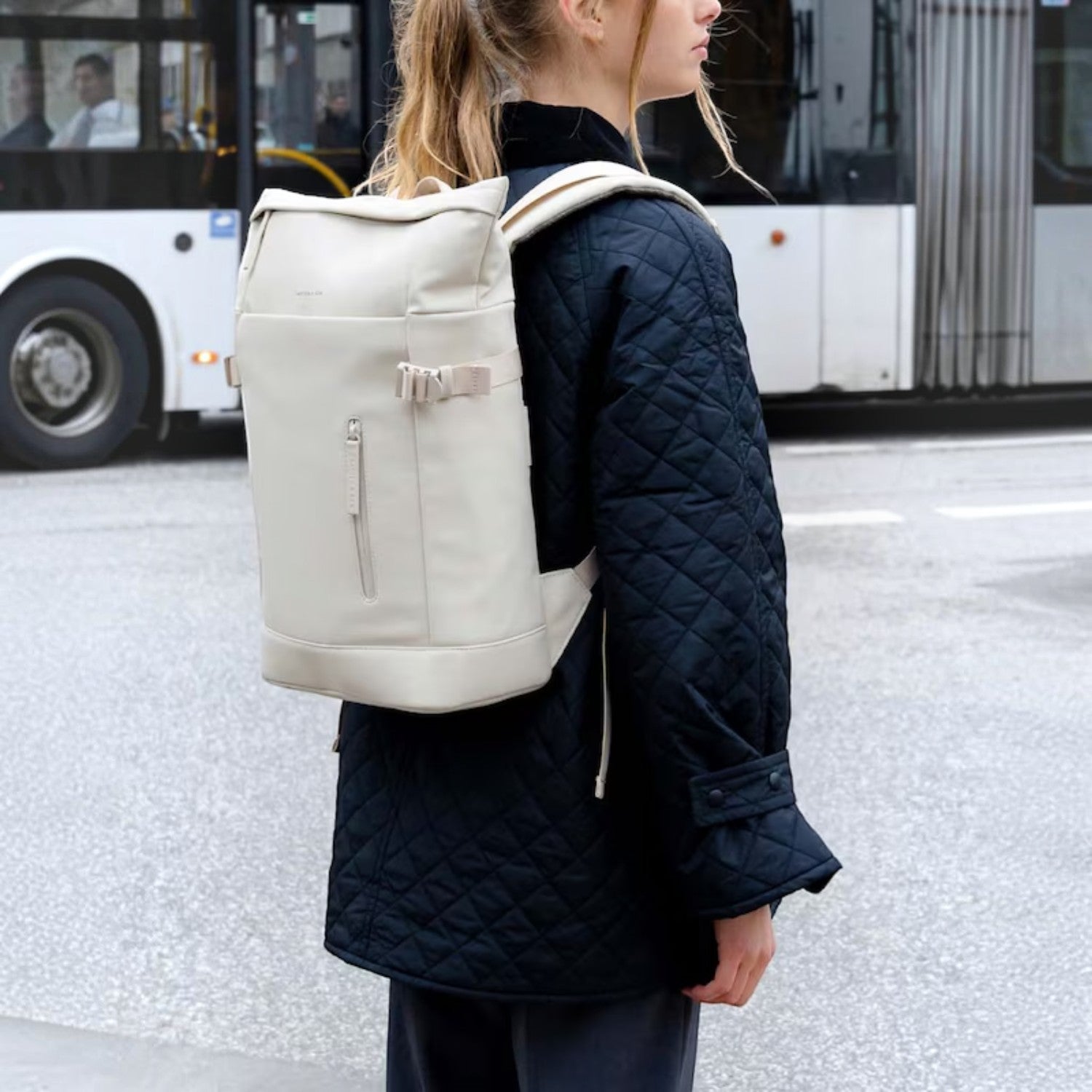Lieblingstasche Helsinki backpack in off-white with a roll-top design, worn by a woman in a black quilted jacket.