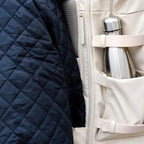 Lieblingstasche Helsinki Pro backpack in beige with a side pocket holding a silver water bottle next to a jacket