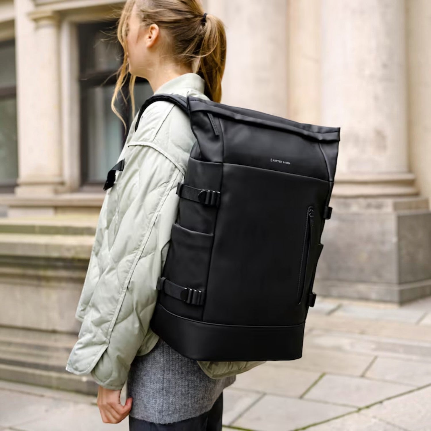 Lieblingstasche Helsinki Pro black rolltop backpack worn by a woman in a light quilted jacket on a city street