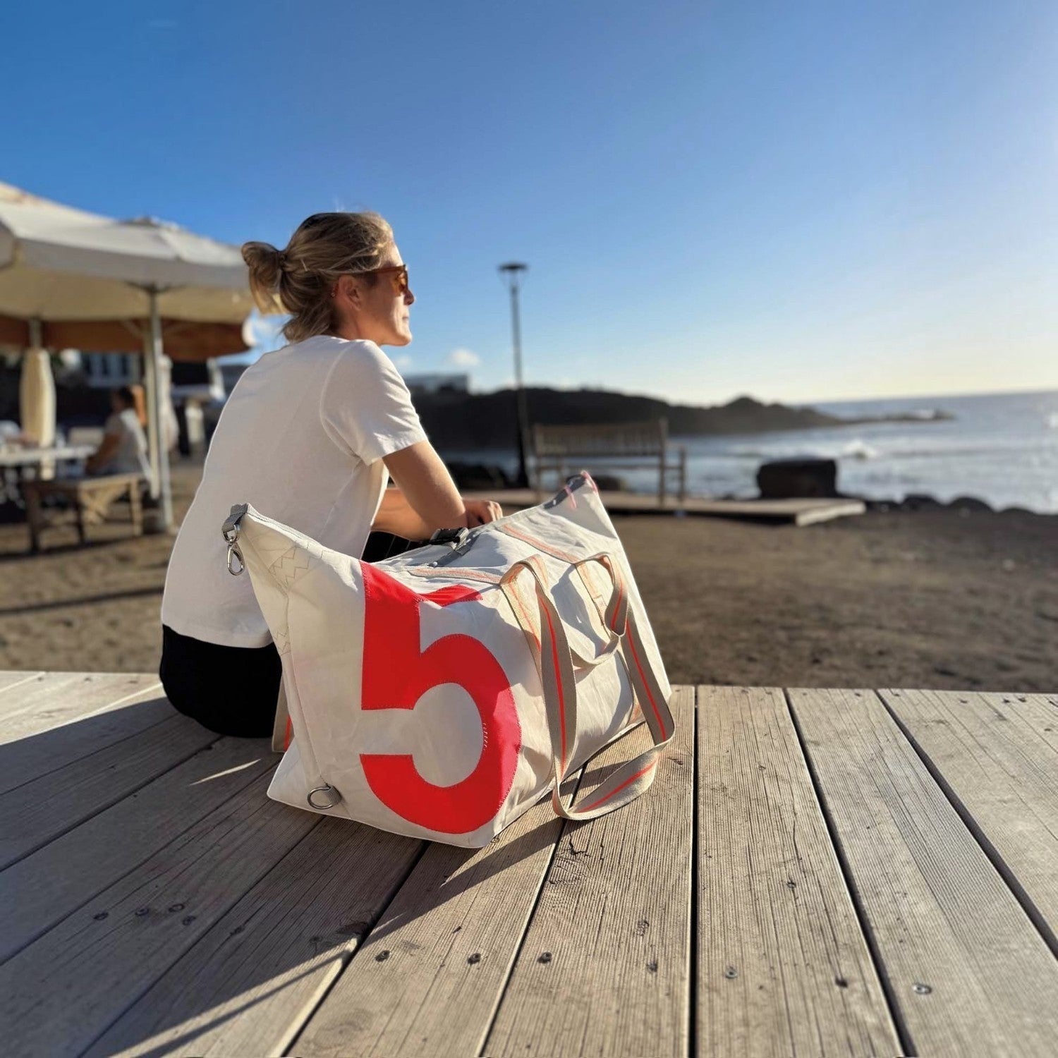 Lieblingstasche Kutter XL sailcloth bag with a large red number 5, resting on a wooden deck by the ocean.