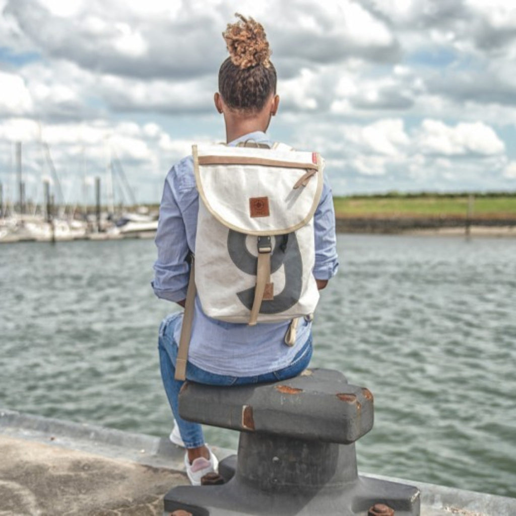 Lieblingstasche Landgang Mini backpack in off-white canvas with a large grey number nine, worn by a woman at a harbor.