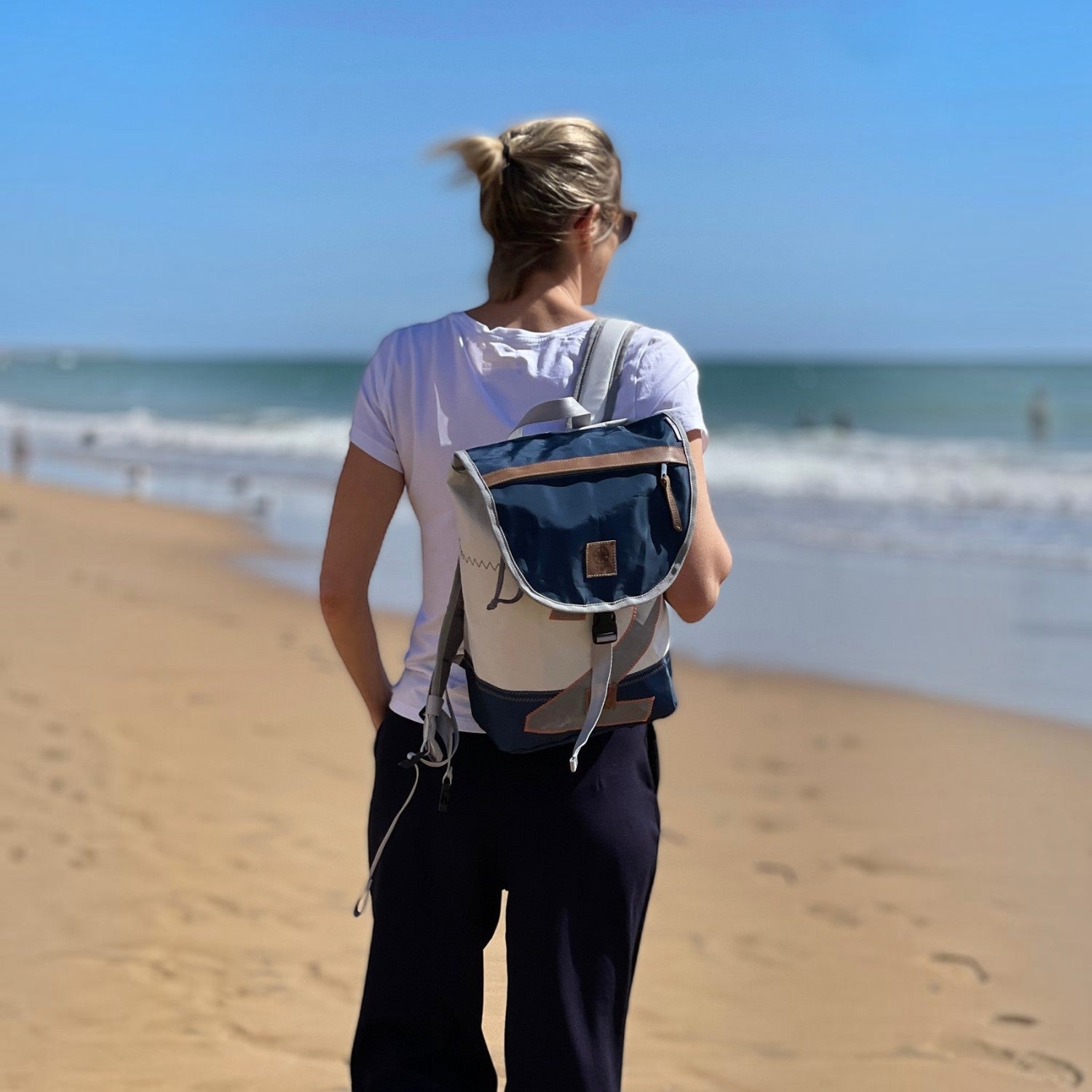Lieblingstasche Landgang Mini backpack made from recycled blue and white sailcloth worn by a woman on the beach