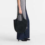 Lieblingstasche Le Foulonné XL shoulder bag in black leather held by a model wearing a grey long vest and jeans.