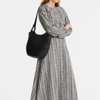 A model wearing a patterned dress carries a black Lieblingstasche Le Foulonné shoulder bag with a curved handle.