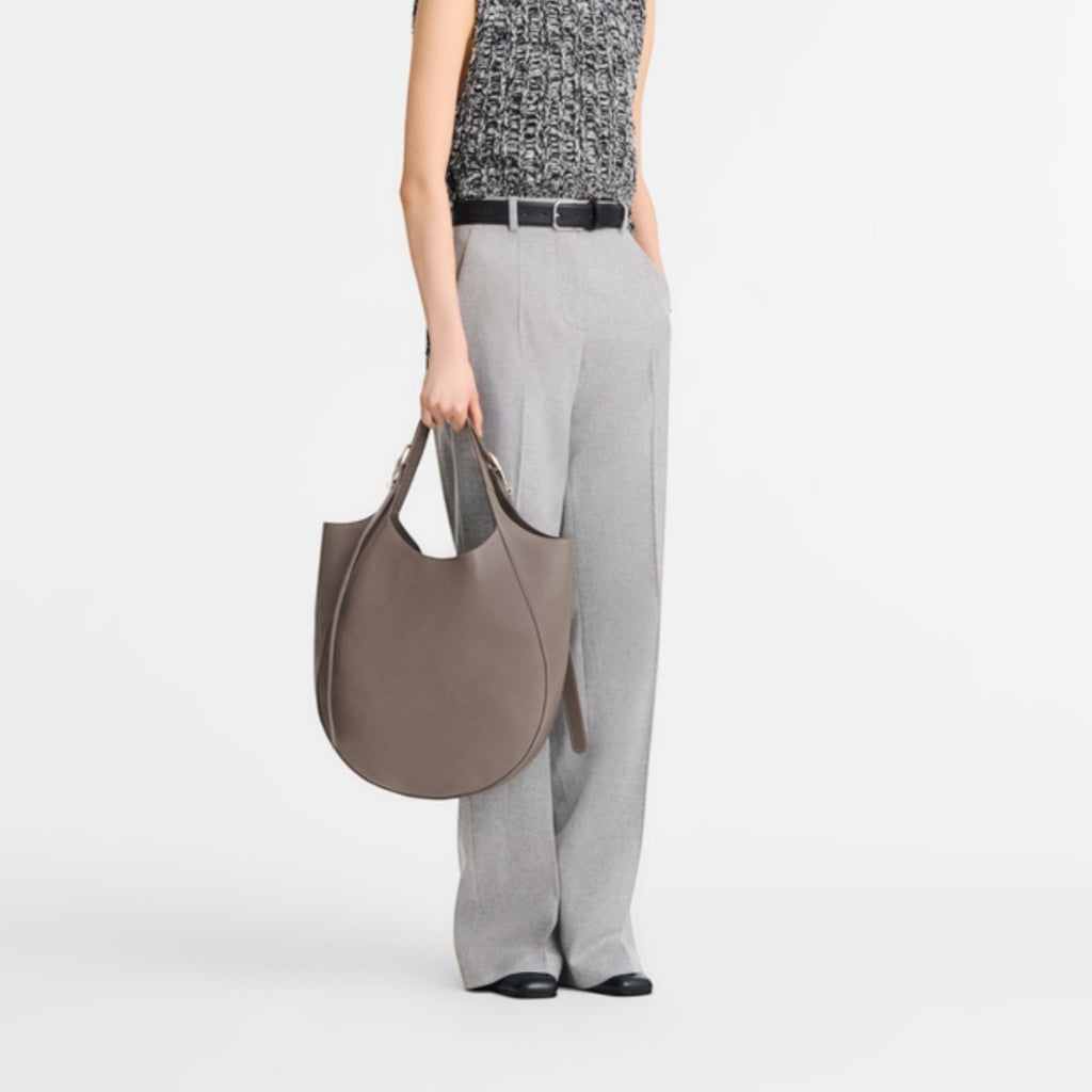 Model wearing grey trousers and a textured top holding a Lieblingstasche Le Foulonné XL taupe leather hobo bag
