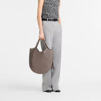 Model wearing grey trousers and a textured top holding a Lieblingstasche Le Foulonné XL taupe leather hobo bag