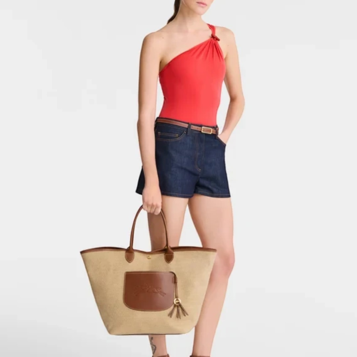Lieblingstasche Le Panier Pliage L shoulder bag in beige straw with brown leather trim held by a model in summer wear