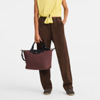 Lieblingstasche Le Pliage Energy medium handbag in burgundy recycled nylon with black rope detail held by a model