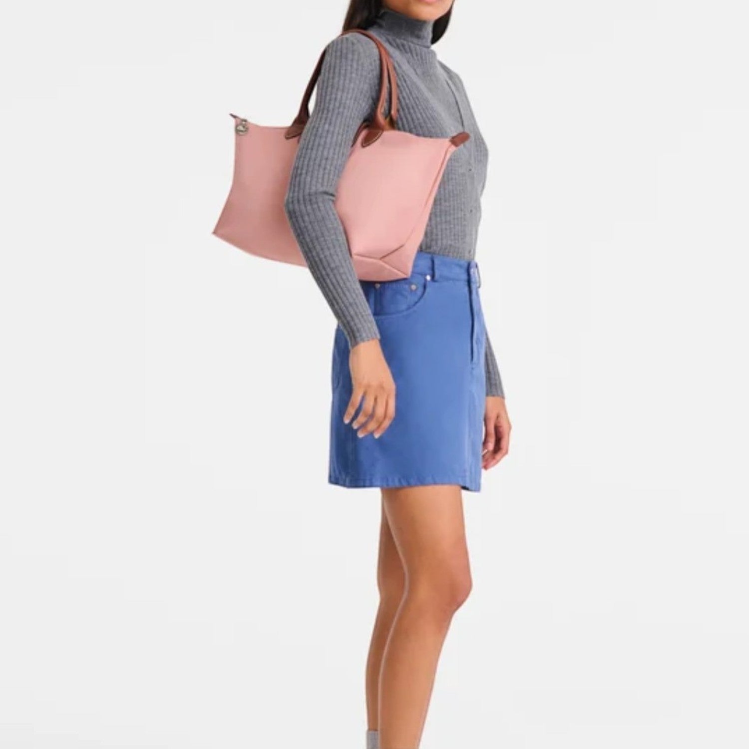 Lieblingstasche Le Pliage L pink nylon tote bag with leather handles, worn by a model in a grey turtleneck and blue denim skirt.