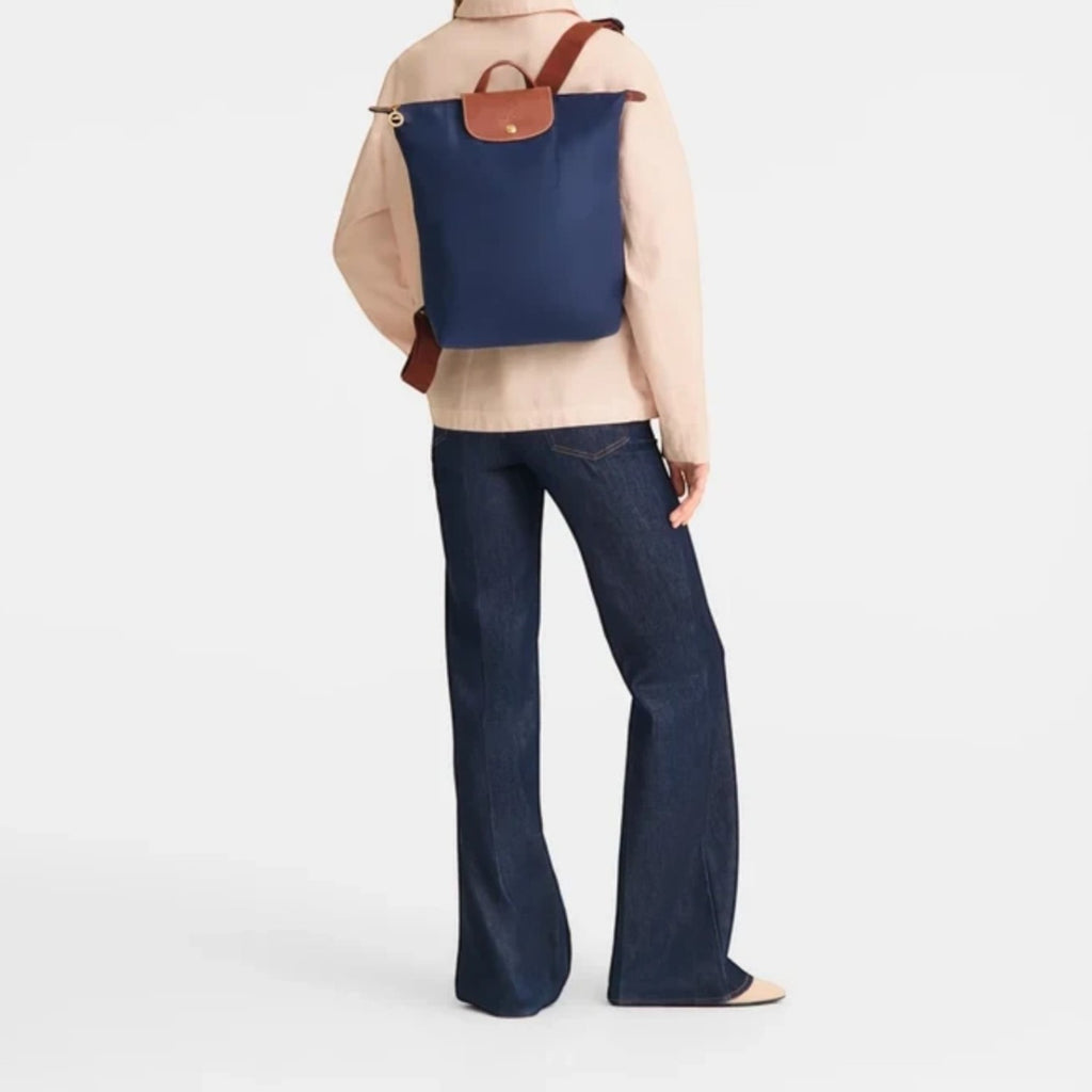 Lieblingstasche Le Pliage navy blue nylon rucksack with brown leather trim worn by a woman in a light jacket