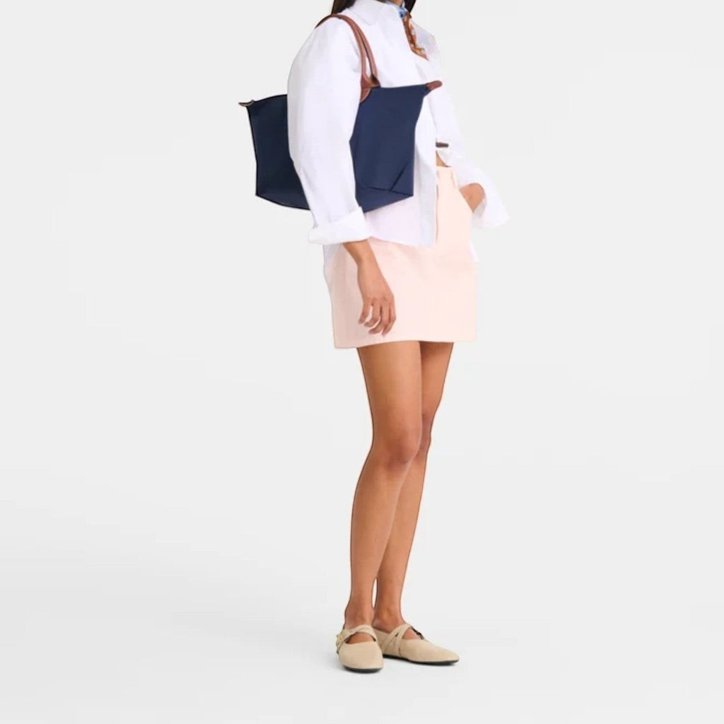 Lieblingstasche Le Pliage L navy nylon tote bag with brown leather handles, worn by a model in a white shirt and pink skirt.