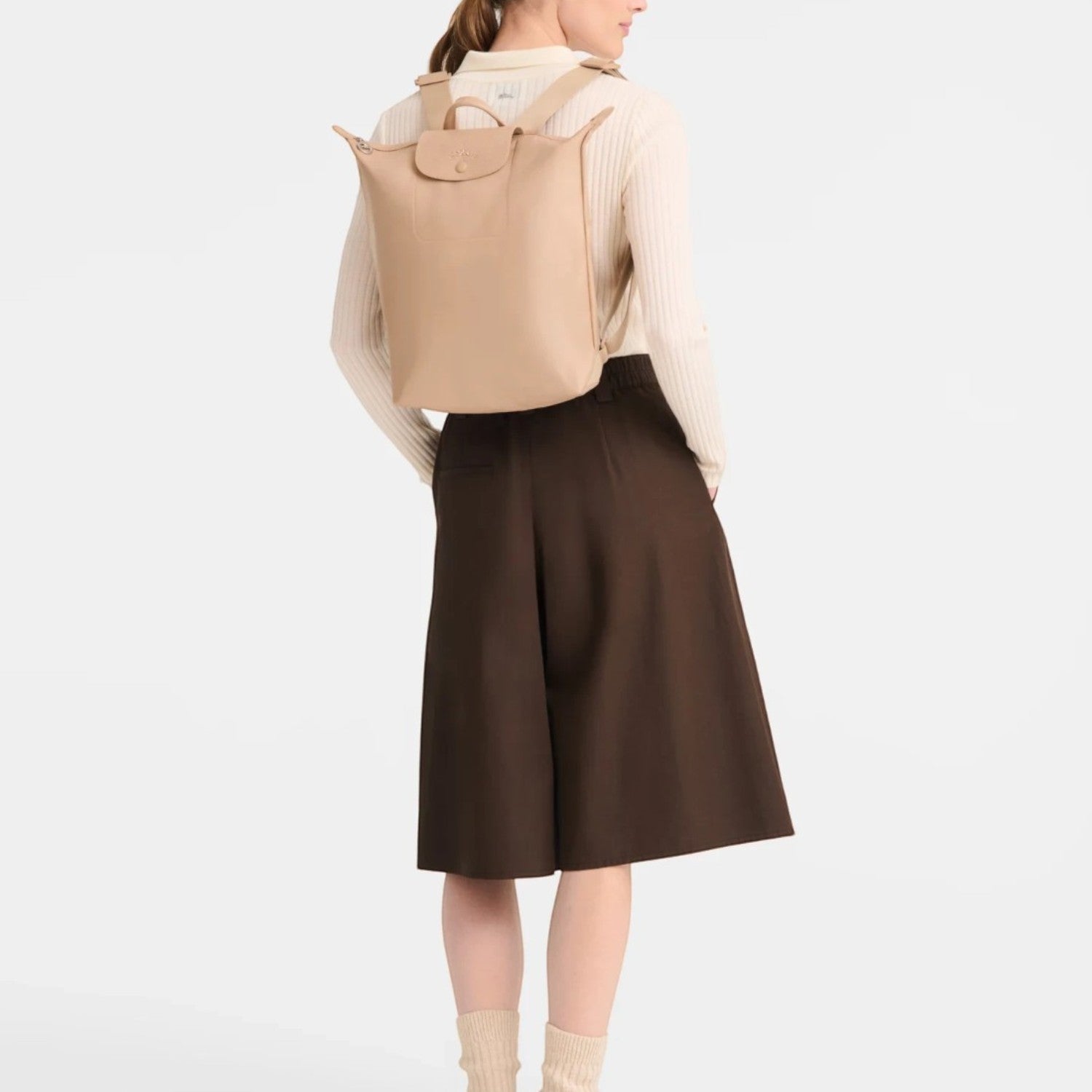 Lieblingstasche Le Pliage One beige rucksack worn on the back by a woman in a cream sweater and brown culottes