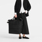 Lieblingstasche Le Pliage One black nylon travel bag with leather trim and handles, worn by a model.