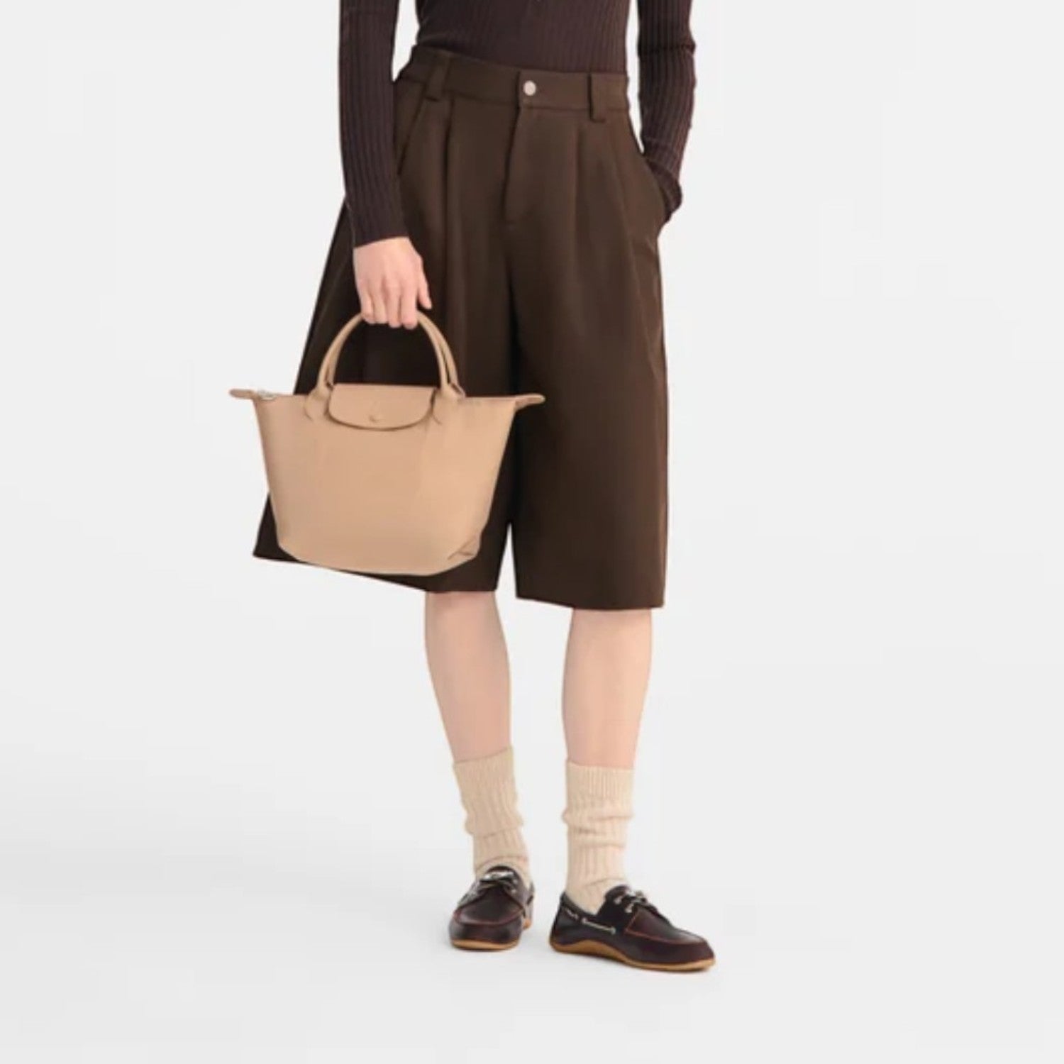 Lieblingstasche Le Pliage One handbag in beige leather, held by a woman in a brown outfit.
