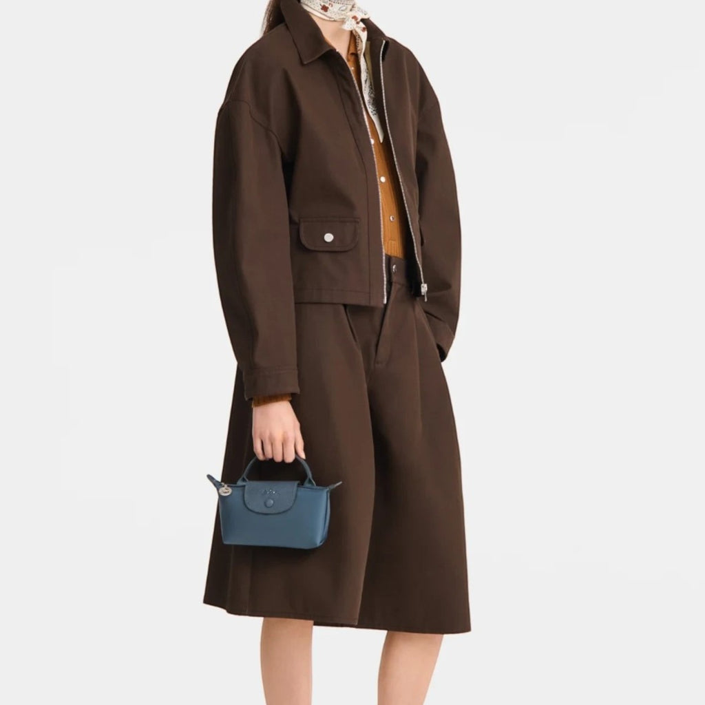 Lieblingstasche Le Pliage One Pochette in blue held by a model wearing a brown jacket and skirt set.