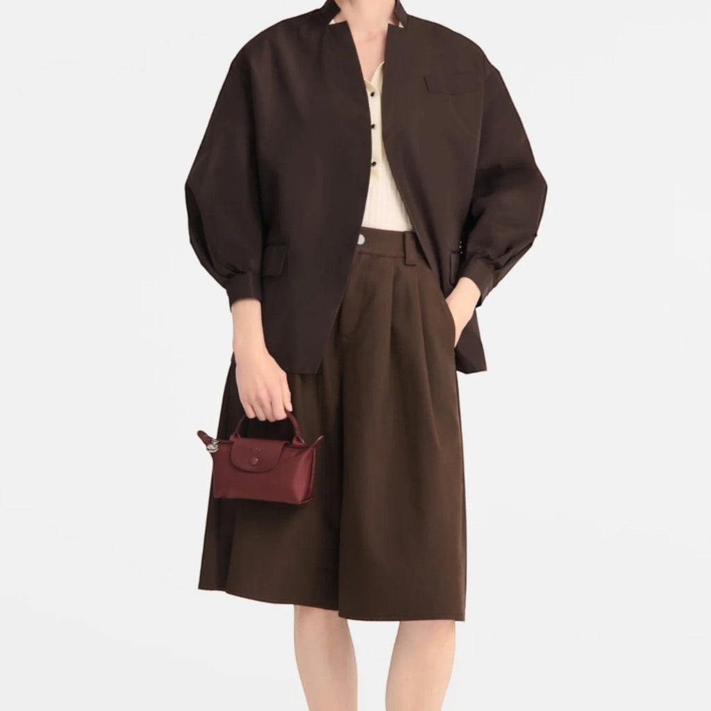 Lieblingstasche Le Pliage One Pochette in burgundy held by a model wearing a brown jacket and matching culottes