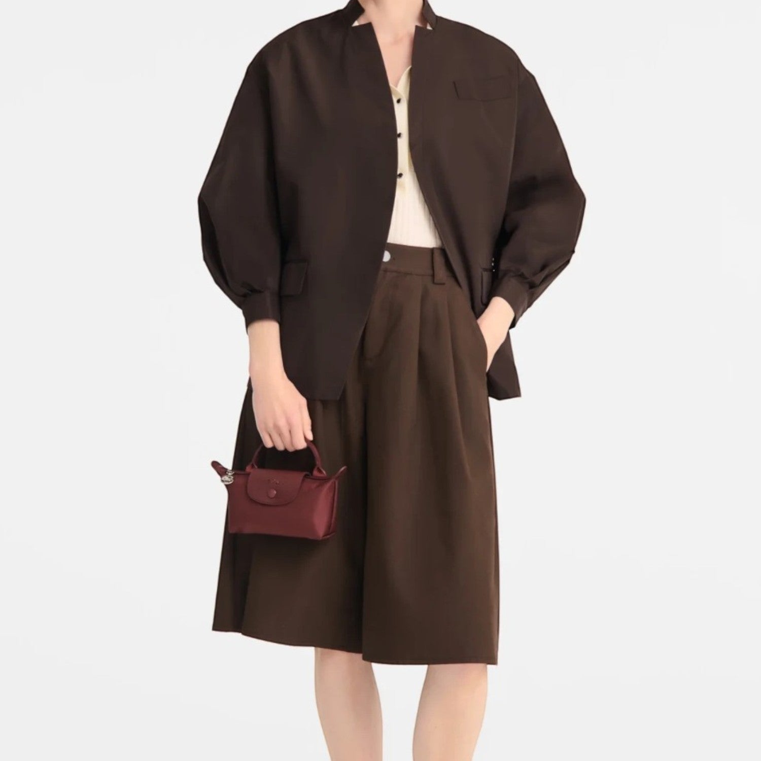 Lieblingstasche Le Pliage One Pochette in burgundy held by a model wearing a brown jacket and matching culottes
