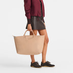 Lieblingstasche Le Pliage One Reisetasche L in beige, held by a model wearing a burgundy jacket and dark skirt.