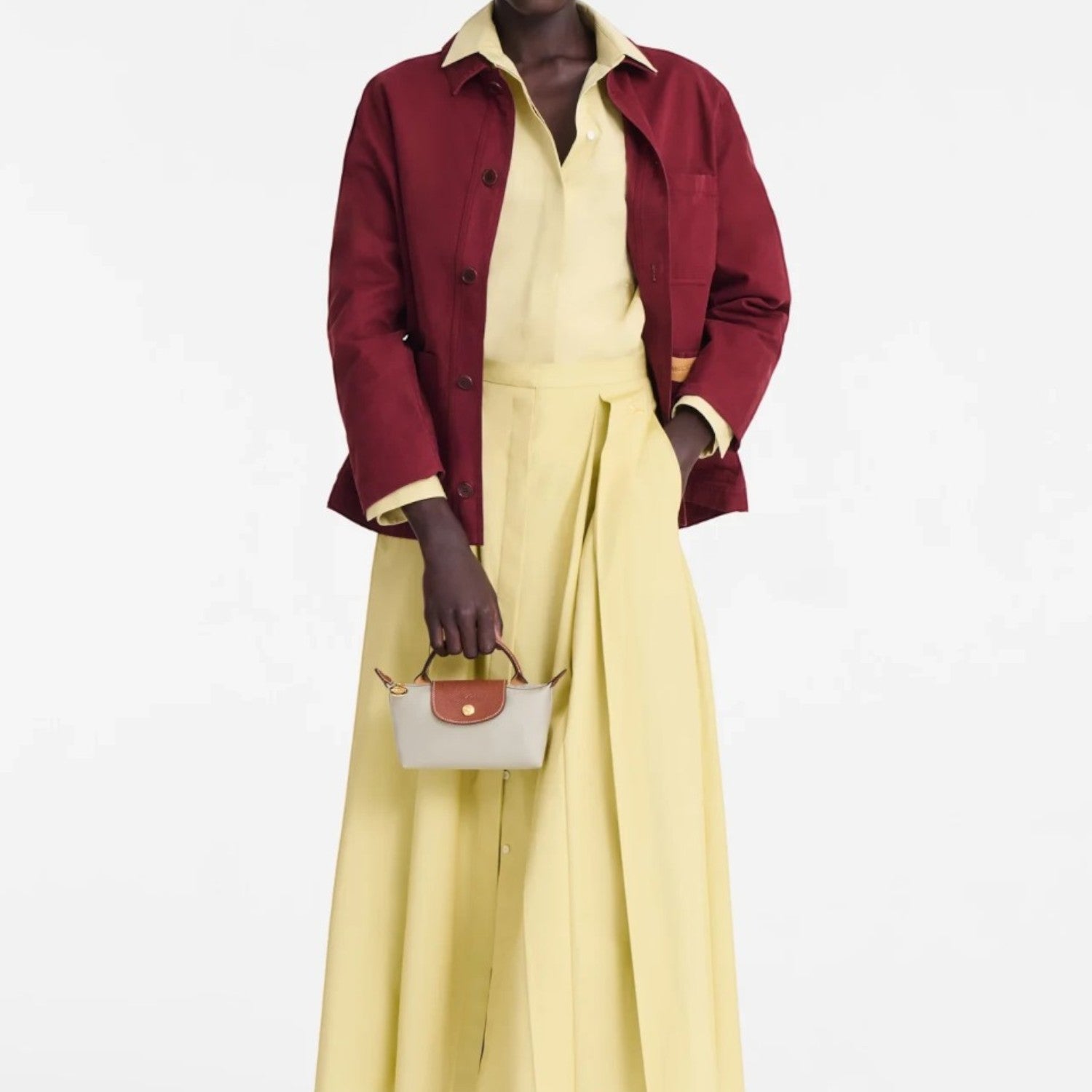 Lieblingstasche Le Pliage Pochette in beige with brown leather handles held by a model in a yellow dress and red jacket