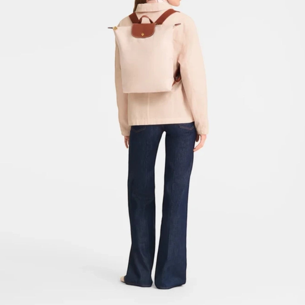 A model wearing a beige Lieblingstasche Le Pliage rucksack with brown leather trim over a light jacket and jeans.