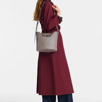Lieblingstasche Le Pliage Xtra medium grey leather crossbody bag worn by a woman in a burgundy trench coat
