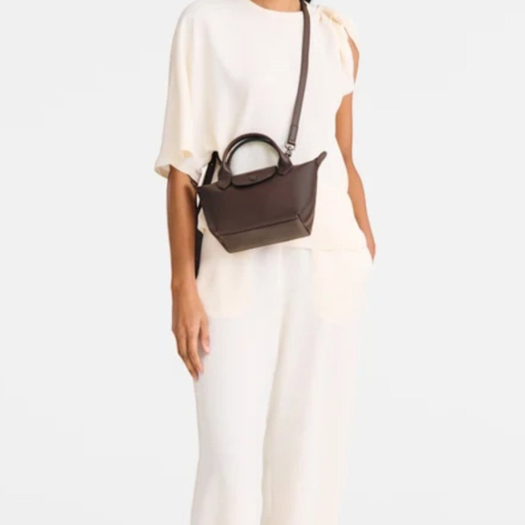 Lieblingstasche Le Pliage Xtra Handtasche XS, a small dark brown leather handbag with top handles and a crossbody strap, worn by a woman.