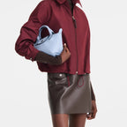 Model holding a light blue Lieblingstasche Le Pliage Xtra XS leather handbag against a white background