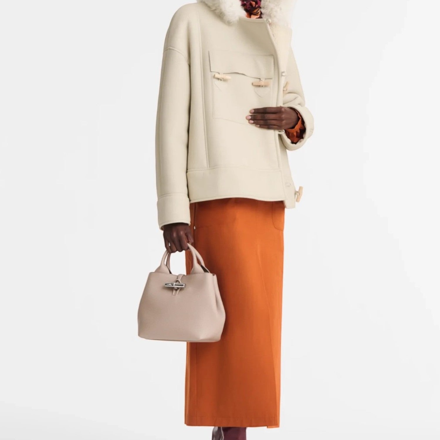 Lieblingstasche Le Roseau Handtasche S in beige leather held by a model wearing a cream jacket and orange skirt