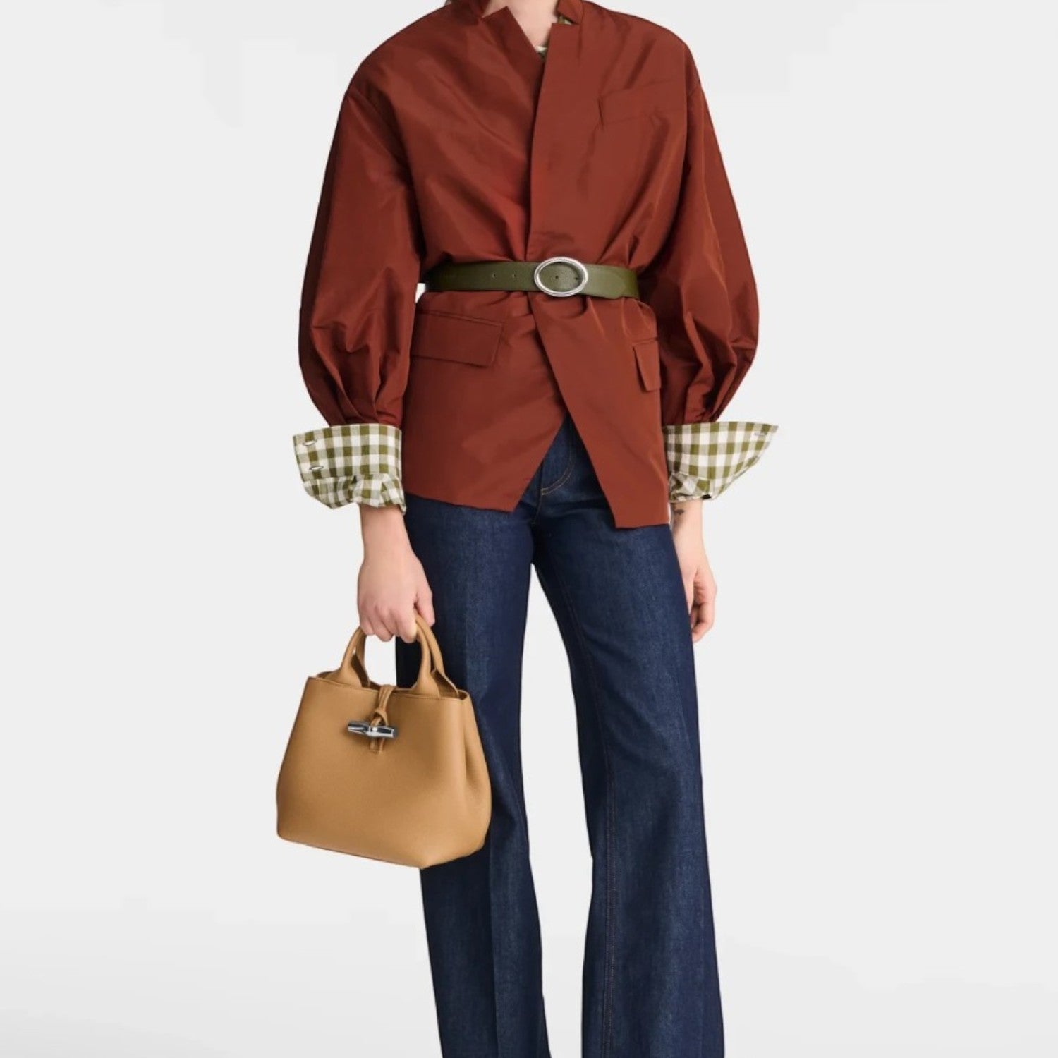 Lieblingstasche Le Roseau Handtasche S in tan leather held by a model wearing a brown jacket and dark blue jeans.