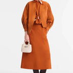 Model wearing an orange suede jacket and skirt holding a small beige Lieblingstasche Le Roseau XS handbag