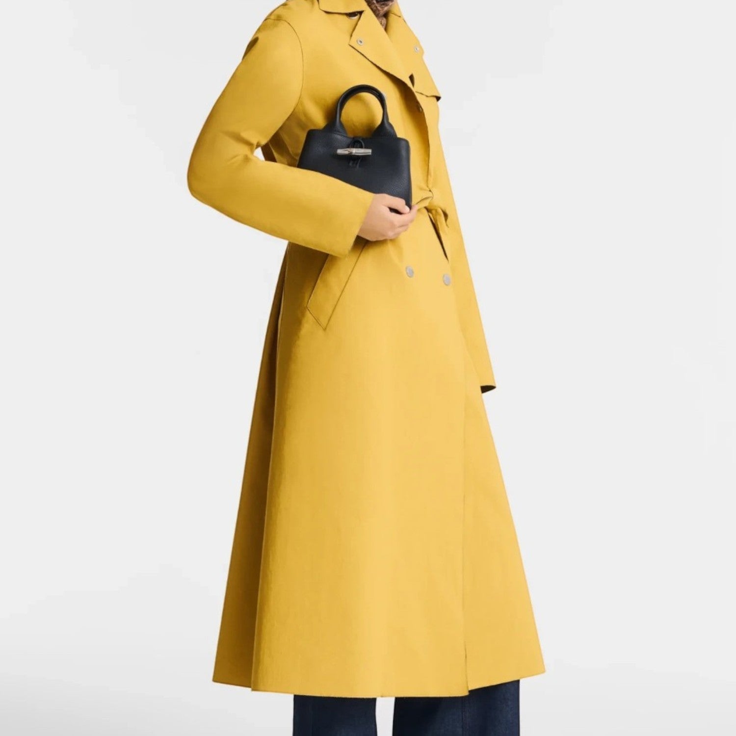 Lieblingstasche Le Roseau XS handbag in black held by a model wearing a long yellow trench coat and wide-leg jeans