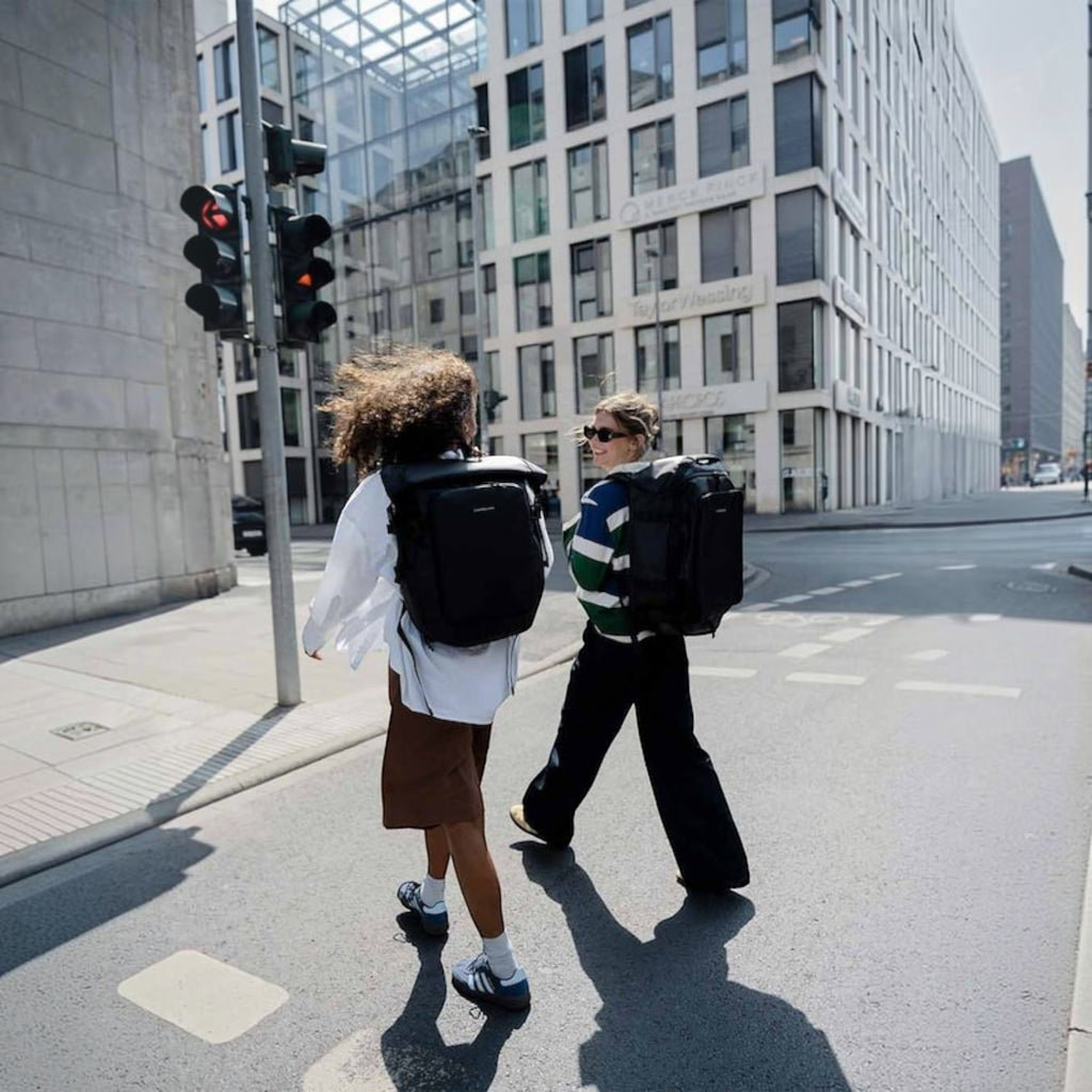 Two people walking in a city wearing Lieblingstasche Lisbon Pro black expandable travel backpacks with ergonomic straps.