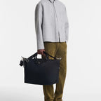 Man holding a black Longchamp Le Pliage Energy travel bag, styled with a grey jacket and olive trousers by Lieblingstasche